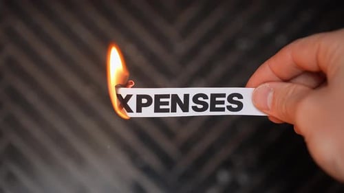 Burning “EXPENSES” concept symbolizing cost savings, lower bills, budget relief, reduced overhead,