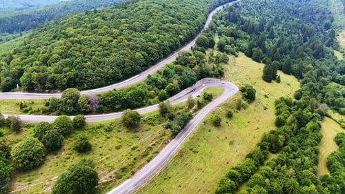 Winding road through lush green hills. A scenic road curves through dense green hills