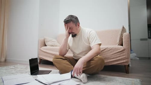 Stressed Man Sitting on Floor with Laptop and Documents