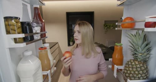 Woman Opens Refrigerator, Eats Brownie and Looks Around