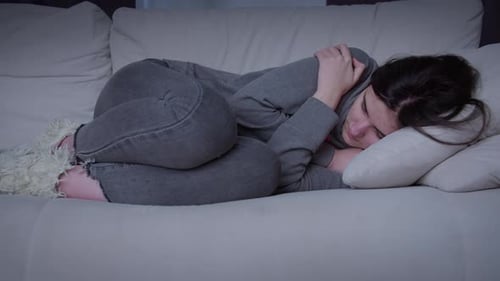 Young Woman Sleeping Curled on Couch at Night