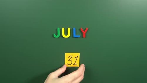 Hand sticking a sticker 31 July calendar day on school board. 31 date of July. Thirty first day
