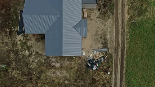 Rural homestead with a corrugated metal roof, adjacent dirt road, clear day drone footage