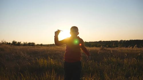 Small Boy Jogging with a Paper Airplane Through Grass Field