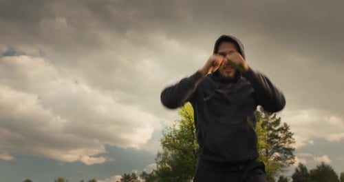 Man Shadowboxing in Field on Cloudy Day