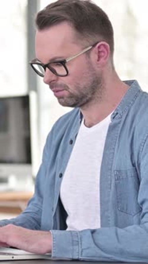 Smiling Man with Glasses Using Laptop Indoors