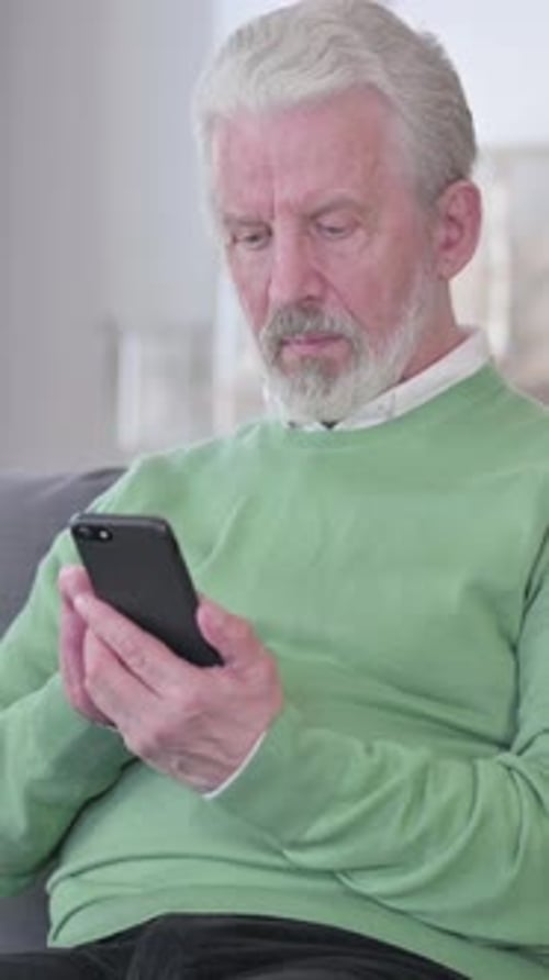 Senior Man Using a Phone Sitting Indoors