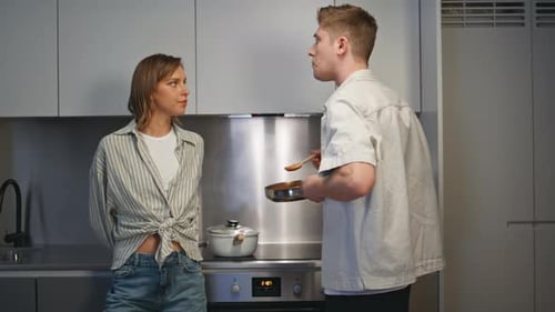 Man Cooks, Offers Taste to Woman in Kitchen