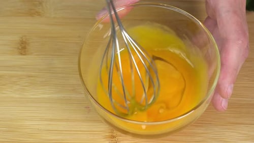 Der Koch verquirlt das ganze Eigelb mit dem Schneebesen in einer Glasschüssel aus nächster Nähe. Lebensmittelvideo, Werbung, Marketing