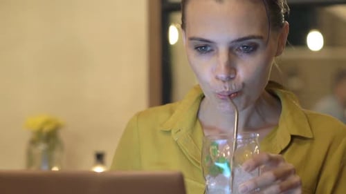 Smiling young woman works on laptop in a cozy cafe at night