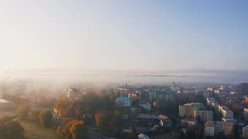 Drone shot of a mist covered town at sunrise, bathed in soft morning sun. Light illuminates the fog