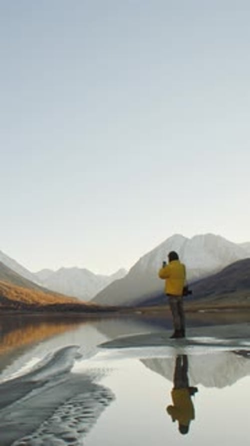 Man Taking Photo with Smartphone By Mountain Lake at Sunrise
