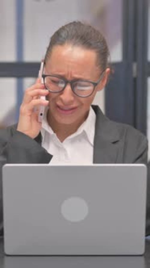 Serious Woman Talking on Phone Working at Computer