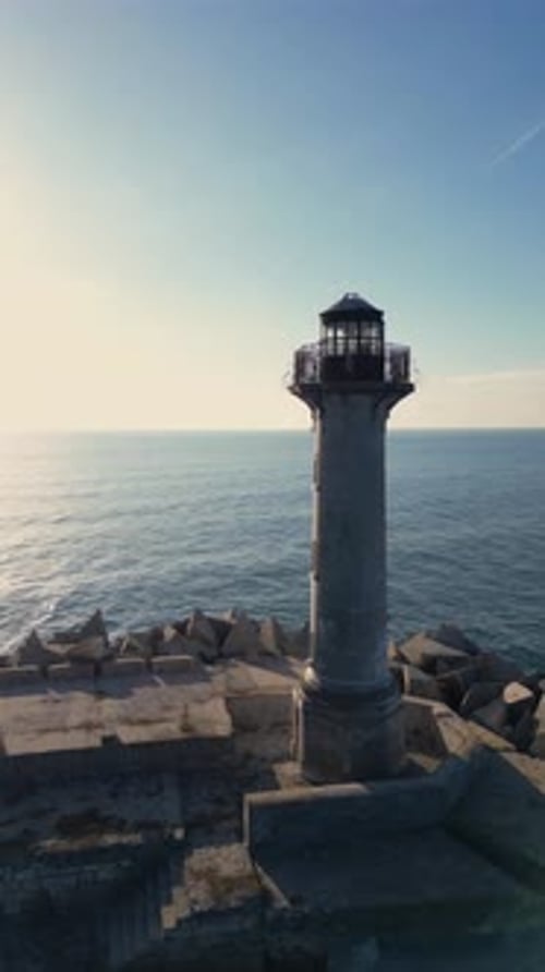 Drone Footage of a Coastal Lighthouse on Rocky Breakwater Scenic Seaside View with Blue Sky Calm