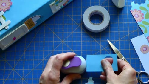 Hands Making Paper Circles on Blue Mat