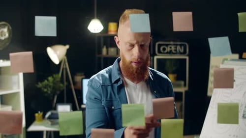 Geschäftsmann klebt bunte Papiere auf eine Glasplatte im Hipster-Büro. Nahaufnahme Lächelnder Hipster Gu...