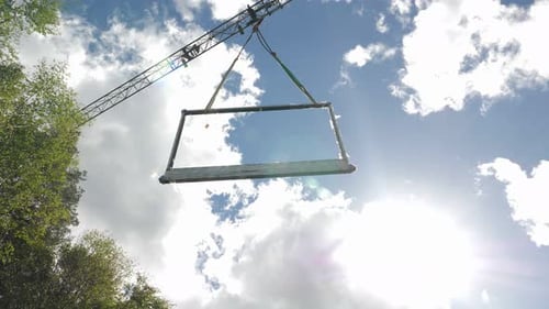 Tower crane carrying window frame against cloudy blue sky