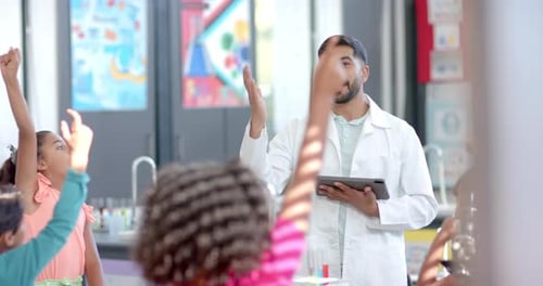 In a school classroom, a biracial teacher holds a tablet in science class
