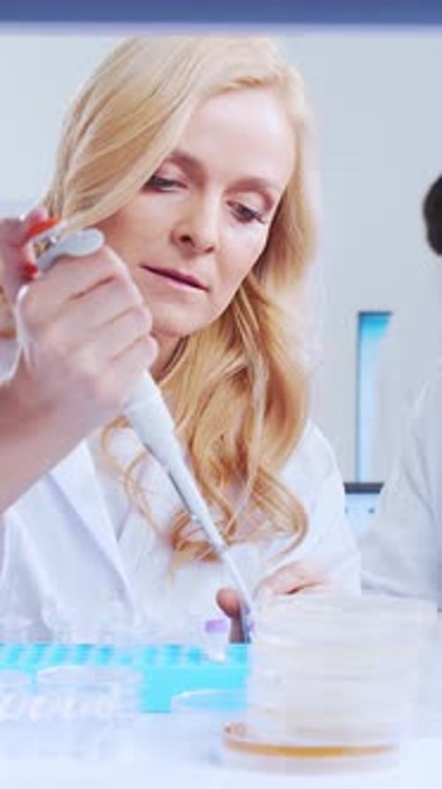 Woman Using Pipette Tool with Associate in Lab