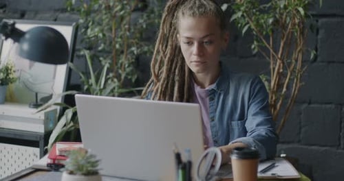 Belle jeune femme avec des dreadlocks travaillant avec un ordinateur portable dans un bureau de style loft créatif