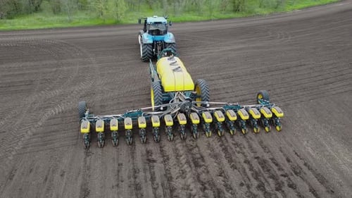 Blue tractor with yellow seeder working on the field in Ukraine OA