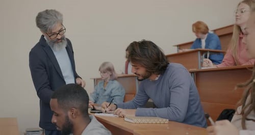 College Teacher Talking to Male Student During Session in Classroom While Men and Women Listening