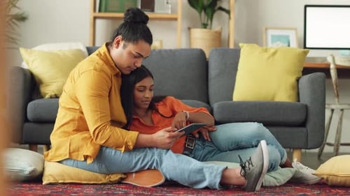 Happy couple together, use a tablet on living room floor, relaxing at their apartment home