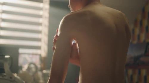 Shirtless Young Adult Rubbing Arms Indoors