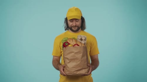 Delivery Man in Yellow Uniform Holding Big Paper Bag with Grocery Food Products Posing at the Camera