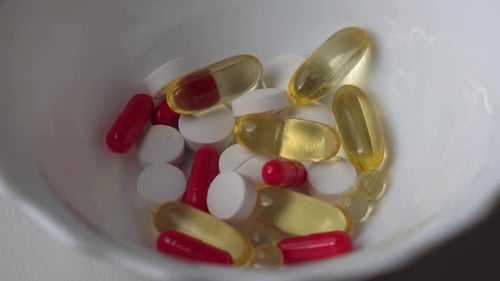 Different colored pills tablets and capsules inside a white ceramic bowl
