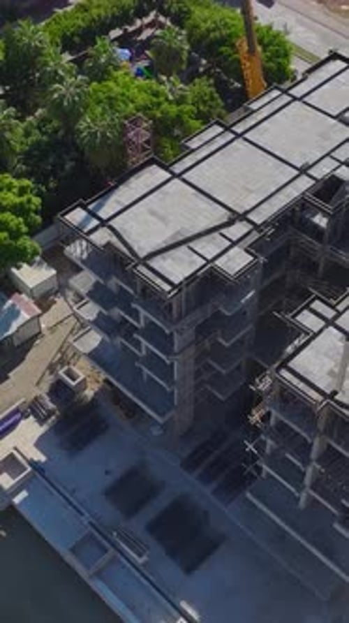 Vídeo vertical del montaje de una grúa torre profesional capturado desde el aire en una concurrida obra de construcción con