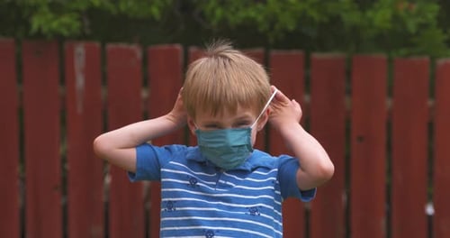 Happy little boy puts on a fabric mask to protect against COVID-19 coronavirus.