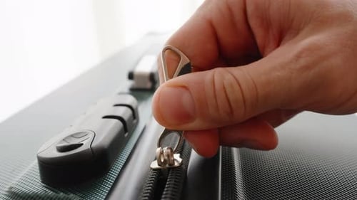 Dolly slider, close up. A Hand unzips a suitcase, marking the beginning of a weekend getaway, filled