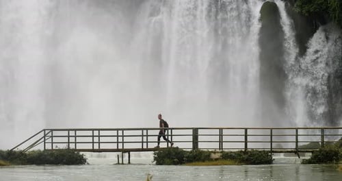 A Backpacker Walking on the Bridge Near a Massive Flow of Stunning Waterfalls