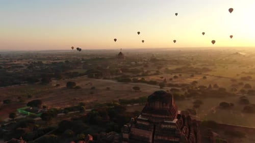 Ancient temple in Bagan, Myanmar with dozens of hot air balloons in background during sunrise. Fly f