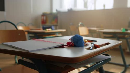 Cuaderno abierto y lápices sobre un escritorio escolar de madera en un aula vacía