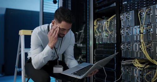 4k video footage of a young man using a laptop and looking stressed while working in a server room