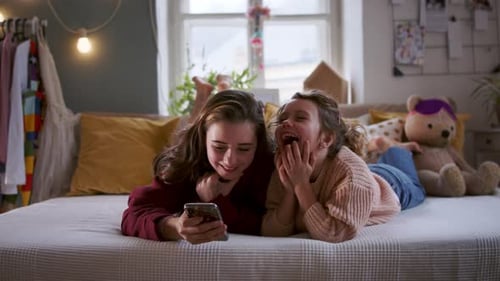 Sisters Laying on Bed Laughing at Phone Content