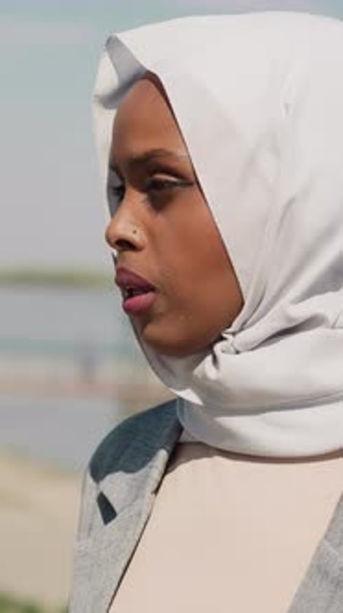 Sorrowing Black Woman with Headscarf Stands on Embankment