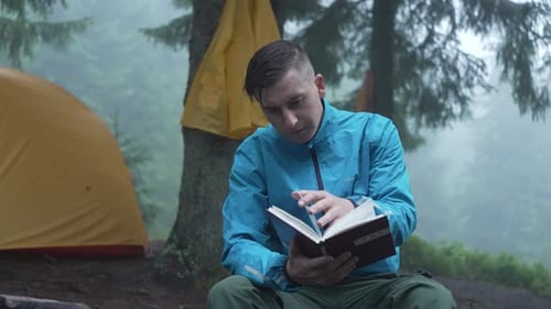 A Man Reads a Book in the Forest in Rainy Weather Camping Near a Tent Fog
