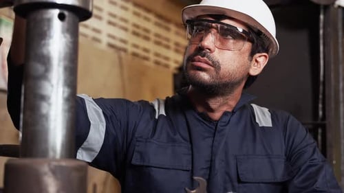 Engineer inspecting complex metal machinery while holding a wrench in a manufacturing plant