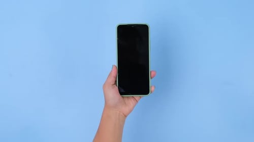 Female hand holding smartphone on pastel blue background in studio.
