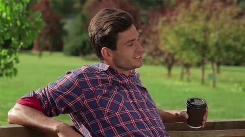 Smiling Man Enjoying Coffee on a Sunny Park Bench