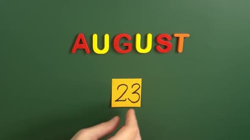 Hand sticking a sticker 23 August calendar day on school board. 23 date of august. Twenty third