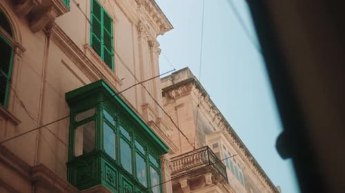 Sunlit Maltese facade with green shutters and traditional balcony