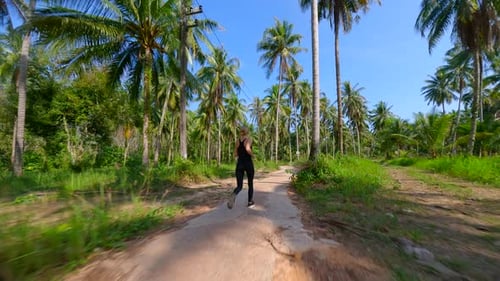 Fitte Frau läuft in Zeitlupe auf der tropischen Straße mit Palmen in Thailand
