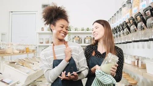 Two female shopkeepers work in zero waste and plastic-free grocery store.
