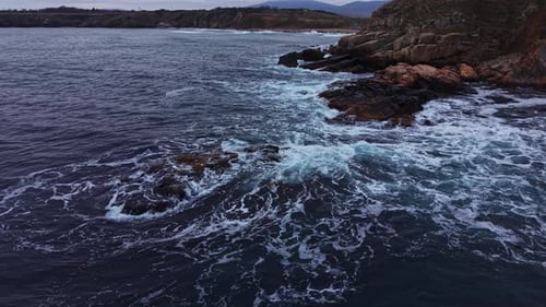 Waves crash against rocky coast near water in coastal area