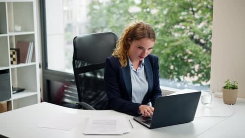 in a Modern Office with a Large Window a Beautiful Worker in a Blue Shirt with a Laptop Looks at the