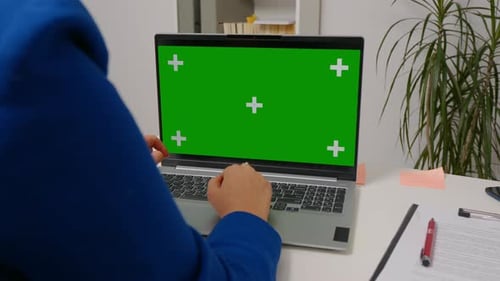 Woman sitting working on laptop with mock up green screen chroma key display.
